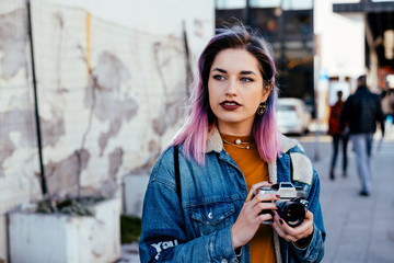 Beautiful young woman photographer holding a camera walking on the street.