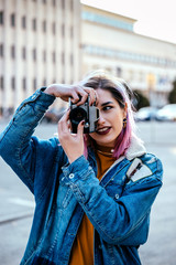 Young woman photographer takes images with camera at city street.