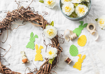 Homemade Easter wreath of vines with flowers, paper rabbits, ribbons on a white background, top view. Easter craft decorations home. Concept of creativity
