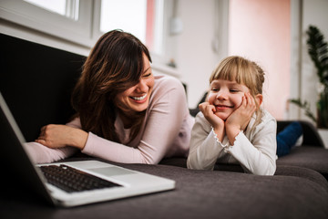 Watching cartoons. Mother and daughter having fun time at home.