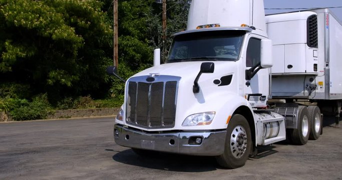 White truck cab pulls away, leaving unhitched white trailer on summer day in rural area. Front view, hand-held real time 4K.