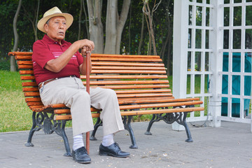 Sad old latin man wearing hat in the summer park.