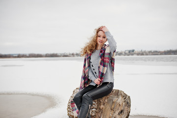 Fototapeta na wymiar Curly blonde girl in checkered plaid against frozen lake at winter day.