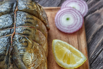 Mackerel smoked fish on a wooden background, close-up, next lemon onion pea pepper, top view.