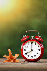 Daylight savings, spring forward concept - red alarm clock and flower - vertical image with blank, copy space