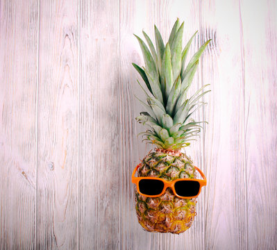 Pineapple in sunglasses over white wooden background