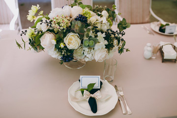 Beautiful and exquisite decoration of the wedding celebration in in the middle of a green garden. Banquet served table with a beige tablecloth, plates, napkins, cards and flower compositions