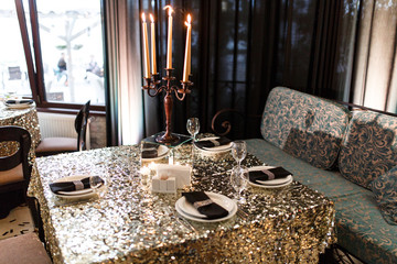 Beautiful decoration of a luxurious wedding banquet in a retro style restaurant. Serving a dining table with a shiny tablecloth, plates, cutlery, glasses, mirror stand and expensive candlestick