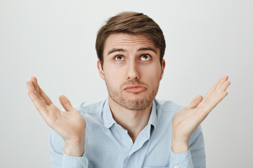 I am not involved, this hands are pure. Indoor portrait of handsome confused guy shrugging with raised palms, looking up and puckering as if making mistake and having no clue how to fix it