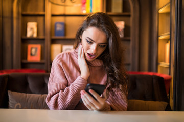 Closeup portrait anxious young girl looking at phone seeing bad news or photos with disgusting emotion on her face cafe background.