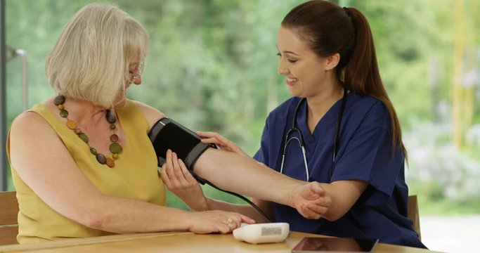 4K Friendly doctor giving blood pressure check to mature lady & looking at computer