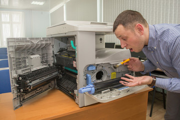 young male technician repairing using a screwdriver and a brush digital photocopier machine