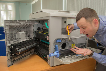 young male technician repairing using a screwdriver and a brush digital photocopier machine