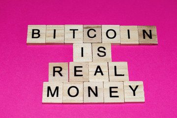 Wooden blocks on a pink background spelling words Bitcoin is real money