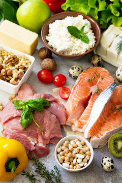 Assortment of a healthy protein source, superfoods on a gray stone background. Meat turkey, salmon, quail eggs, dairy products feta cheese and cottage cheese, beans, spinach, chickpeas, fruit.