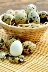 Quail eggs in basket with straw on wooden background