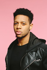 Obraz premium Portrait of a serious urban African American man in black isolated on pink background