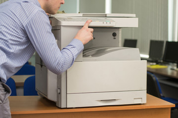 a young office manager wonders or is surprised at the work of a multifunction printer or copier