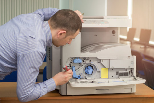young male technician repairing using a screwdriver and a brush digital photocopier machine