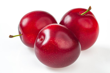 Close-up sweet red plums with leaves, and a juicy plum cut into a half, isolated on white