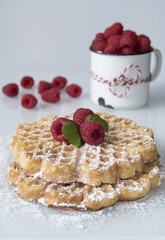 Frisch gebackene Herz WAffeln mit Puderzucker und frischen Himbeeren im Hintergrund