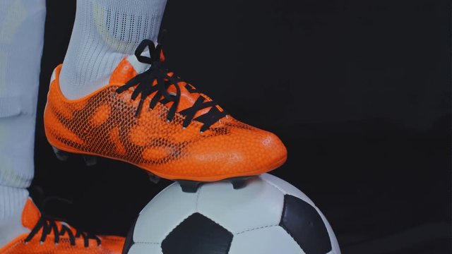 Footballer In Boots Stop A Ball And Putting His Leg On It, Black Background