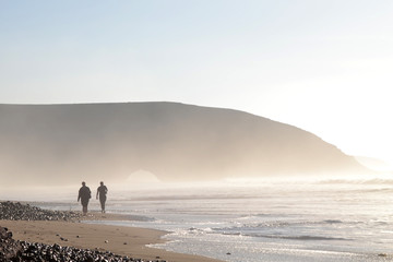 Two tourists walk along the coast of Legzira beach. View of the famous first arch.