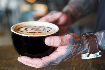 Tattooed hands holding Coffee in Rustic setting