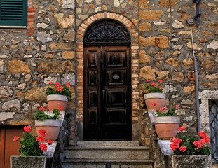 Fototapeta na wymiar Old wooden door decorated with flowerpots and steps in medieval town, Tuscany, Italy