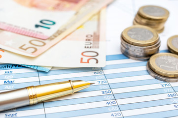 Euro bills and coins with pen on the financial graphs. Business concept.