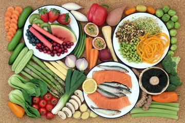 Health food for healthy eating concept with fresh fish, vegetables and fruit on cork background. Healthy food concept high in omega 3, antioxidants, anthocyanins, minerals, vitamins and dietary fibre.
