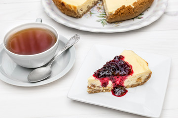 Cup of tea with piece of cheesecake with jam on the table.