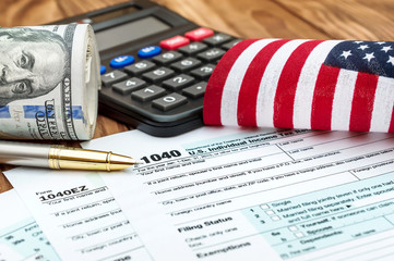 Tax forms with small american flag, calculator nad roll of dollar bills on the table. Business...