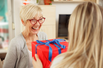 Young woman giving red gift box to her mother. Mother's day. Happy family moments at home