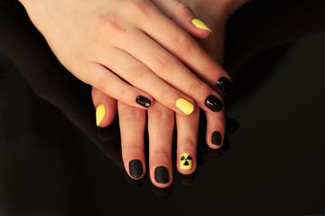 beautiful black-and-yellow manicure with shellac varnish in the form of a sign of radioactive danger. hands of the girl on a black shiny background