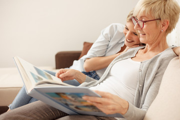 Mother and daughter having a great time while looking through old family photo album. Happy family moments at home