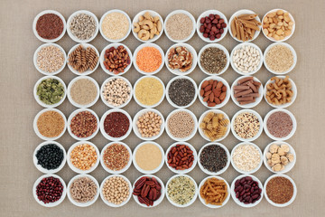 Vegan high protein dried super food selection with nuts, seeds, legumes, cereals and grains. Health foods high in fibre, antioxidants, anthocyanins, minerals and vitamins. On hessian, top view.