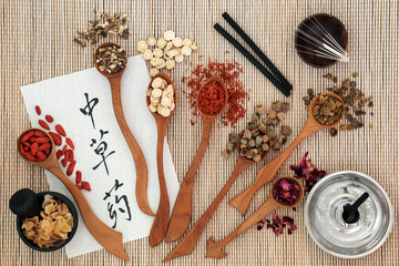 Chinese acupuncture needles and moxa sticks used in moxibustion therapy with herbs and calligraphy script on rice paper. Translation reads as chinese herbs. Top view on bamboo.