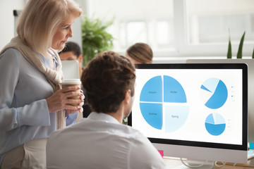 Statistics data team analysis concept, senior serious executive checking annual financial report on computer screen helping colleague in project strategic planning, analyzing work result, teamwork