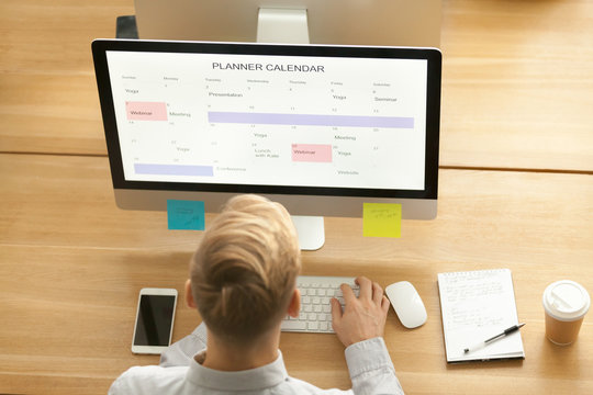 Young Man Using Planner Application On Pc Computer In Office, Businessman Planning His Day Making Events Schedule With Organizer Calendar App On Desktop Screen, Time Management Concept, Top View