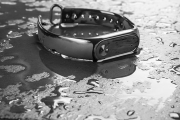 Fitness bracelet on a black slate background with drops of water