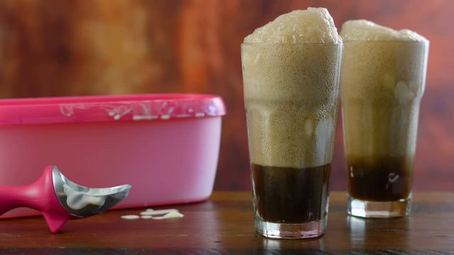 Preparing black cow cola ice cream soda floats against rustic wood background.