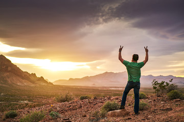man watching amazing sunset cheering with raised arms in the air