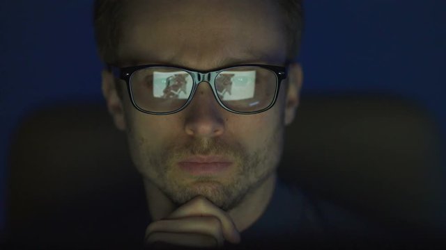 The serious man in glasses working near the monitor. evening night time