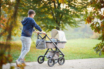 Man with baby stroller walks in the autumn park at sunset