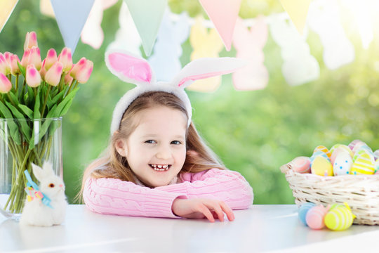 Funny little girl in bunny ears at breakfast with Easter eggs basket.