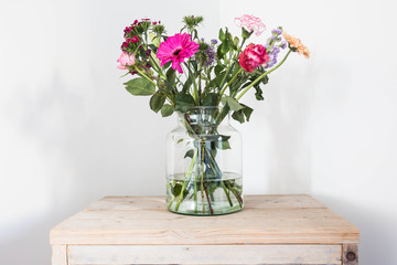 Colorful flowers in vase, spring decoration on wooden table white wall