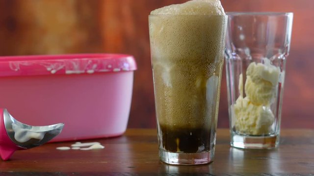Preparing black cow cola ice cream soda floats against rustic wood background, time lapse.