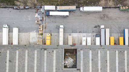 Perpendicular aerial view of a warehouse and its roof. In the parking lot some trucks load and unload the products.
