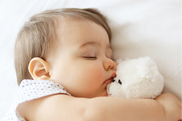 Sweet little baby sleeping and hugging white teddy bear, close-up